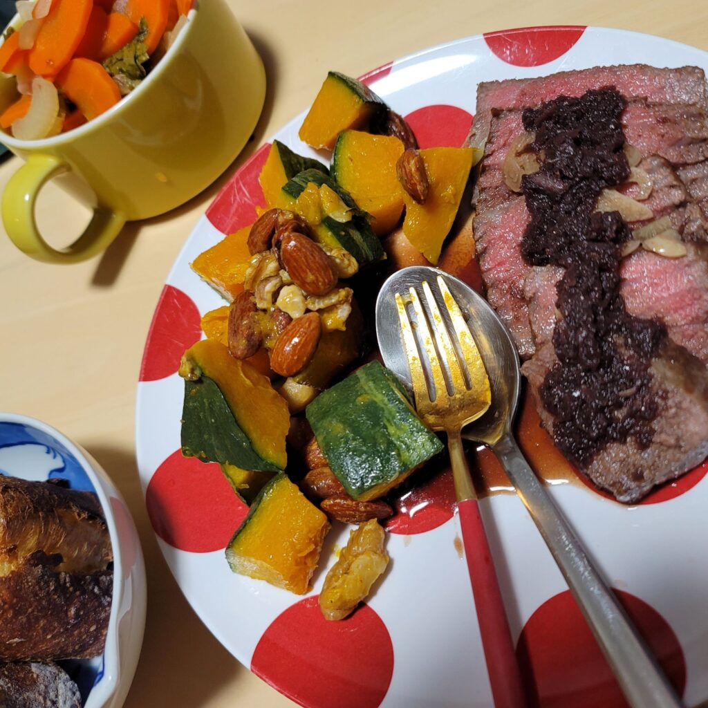 ローストビーフ、かぼちゃとナッツの副菜、にんじんとセロリのスープ、バゲットの写真。
ローストビーフには茶色いソースがかかっている。